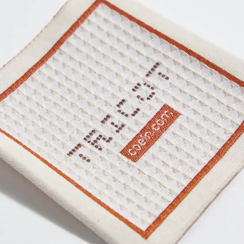 Etichetta a cavallotto tessuta a punto lavorato, design elegante e resistente per abbigliamento e accessori di alta qualità.